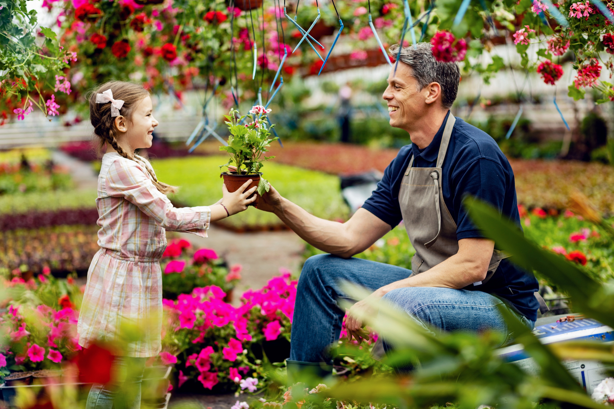 Beautiful flower for my beautiful little girl! Happy father giving his small daughter potted flower while she's helping him in a garden center.