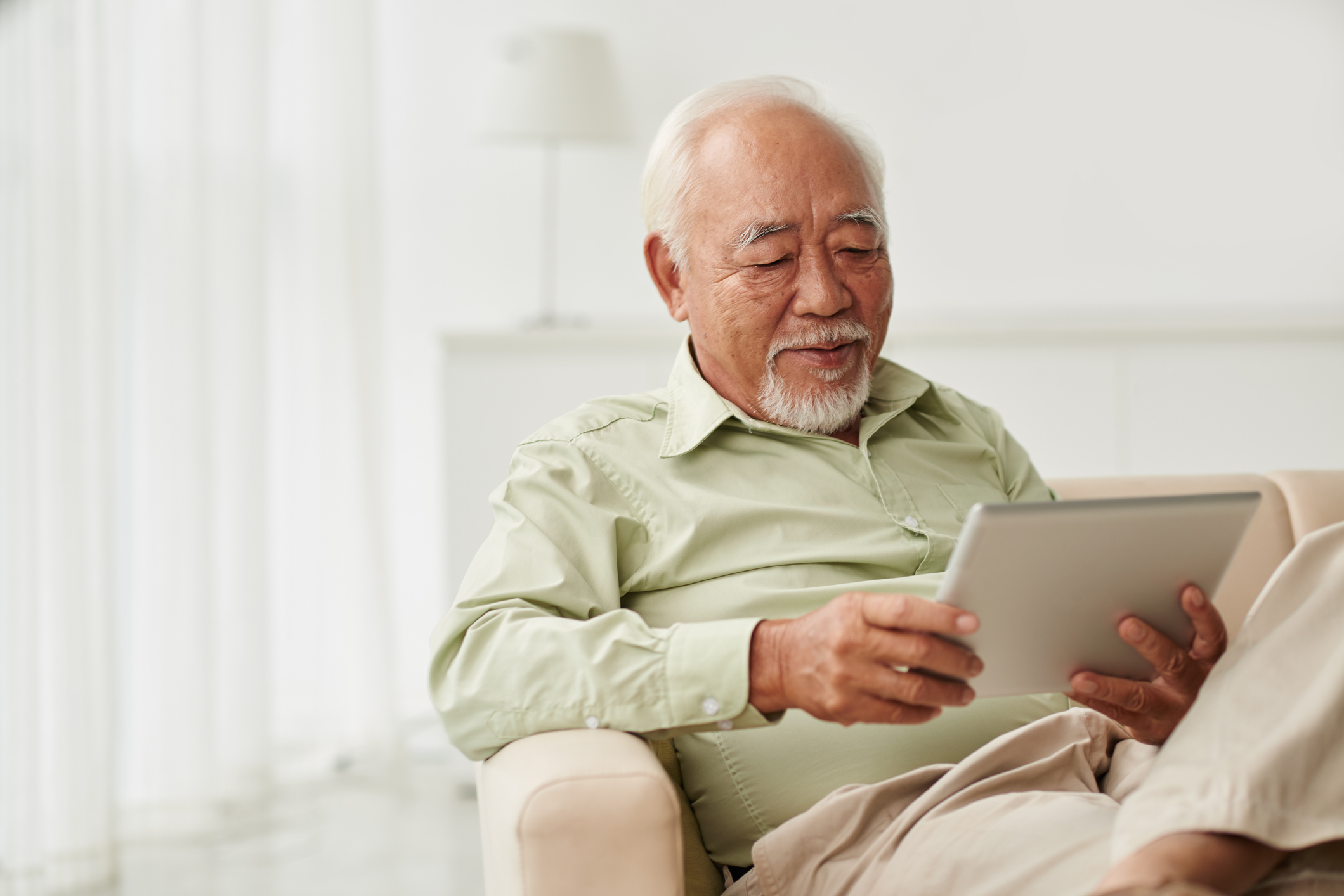 Reading news Senior Vietnamese man sitting on sofa and reading new on his tablet computer